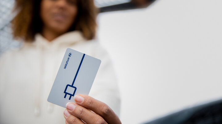 A woman holds up a Charge myHyundai charging card.