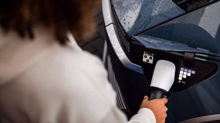 A woman charging an electric Hyundai car using a charging cable connected to the car's port on a rainy day.