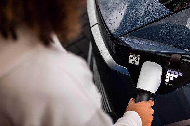 A woman charging an electric Hyundai car using a charging cable connected to the car's port on a rainy day.